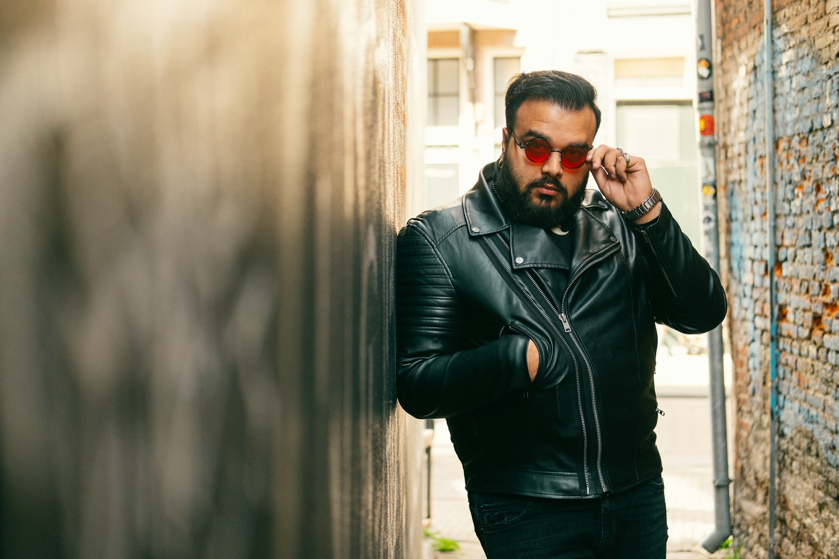 Man in a black leather biker jacket leaning against a wall